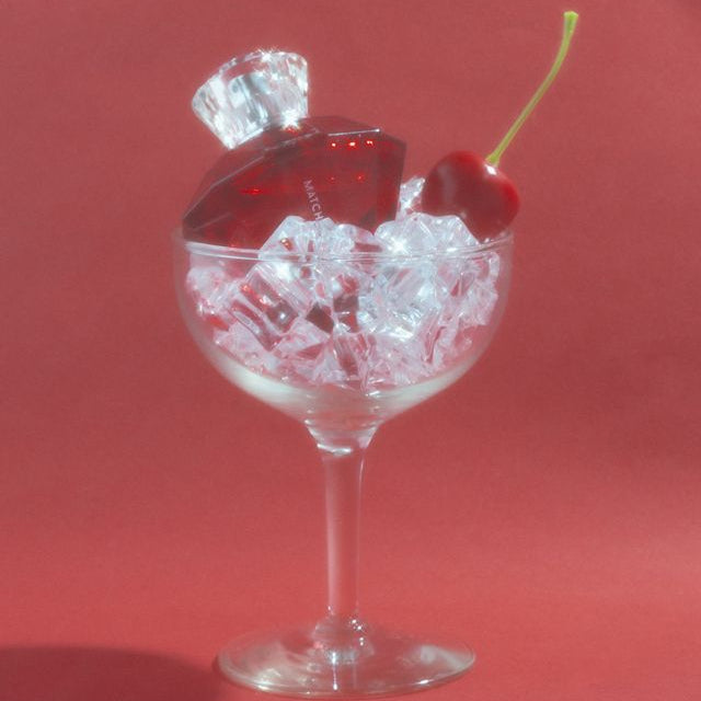 Matchmaker perfume in a cocktail glass with crystal ice cubes and a red cherry on a stalk.