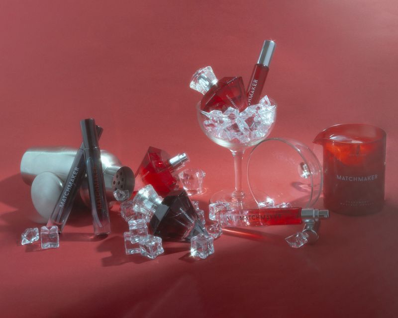 Matchmaker cologne, perfumes, and a massage candle displayed in cocktail glasses with a cocktail shaker and crystal ice cubes.